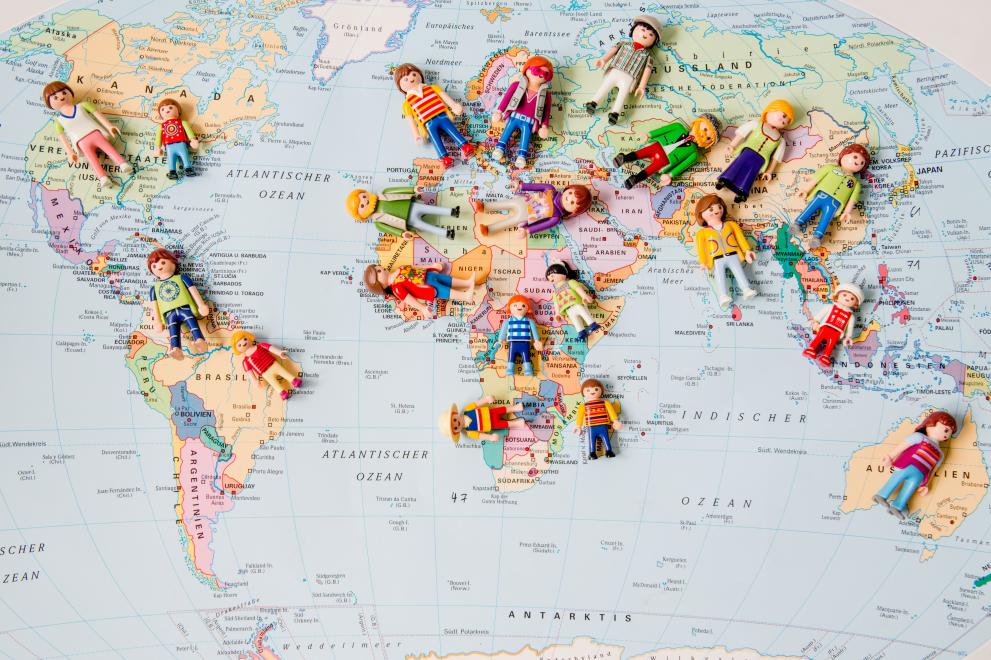 Weltkarte mit liegenden Playmobilfiguren auf den Kontinenten